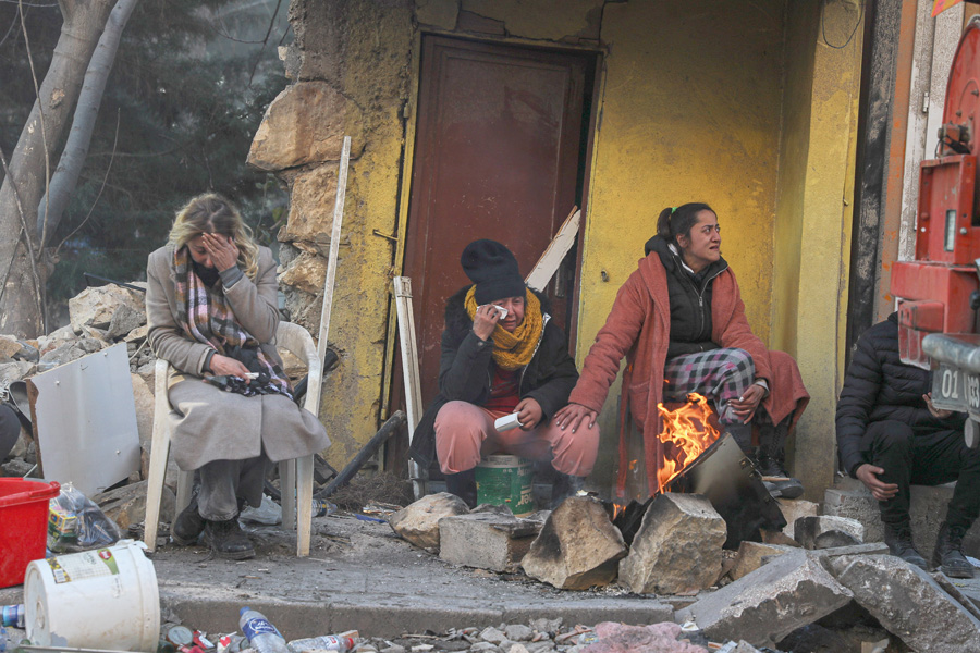 People sit by the debris of their collapsed house